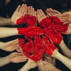 Dłonie pomalowane na czerwono tworzą serce, symbolizując wspólny altruizm i pomoc.