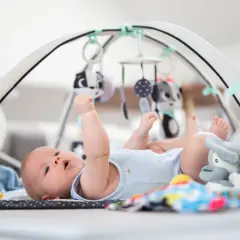 Niemowlę leży na macie sensorycznej pod łukiem z zabawkami.