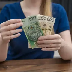 Dłonie trzymają banknot 100 zł i dwa po 200 zł. Łącznie 500 zł, czyli połowa z 1000 plus.