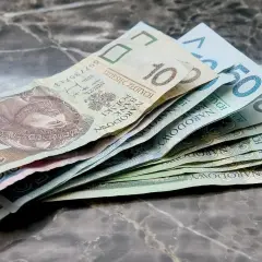 Złotówki na marmurowym blacie. Widać banknoty 10, 50 i inne, które mogą pomóc w pokryciu kosztów związanych z zasiłkiem rodzicielskim.