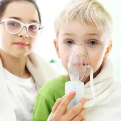 Chłopiec z maską inhalacyjną na twarzy, wspierany przez siostrę. Dzieci przechodzą inhalację z soli fizjologicznej.