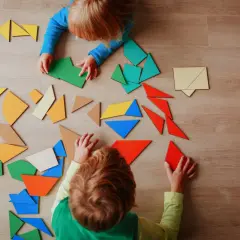 Dzieci układają kolorowe klocki tangram. Widać ich skupienie podczas zabawy.