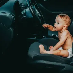 Maluch w pieluszce siedzi za kierownicą, jakby zastanawiał się, od kiedy dziecko może jeździć z przodu.