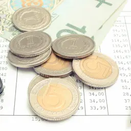 Kalkulator, monety i banknoty na tle dokumentu z wyliczeniami. Może to być pomoc w rozliczeniu zasiłku dla samotnej matki.