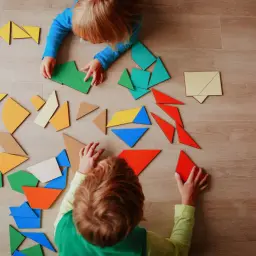 Dzieci układają kolorowe klocki tangram. Widać ich skupienie podczas zabawy.