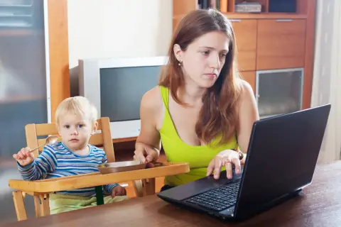 Pracująca mama z dzieckiem przy stole. Widać, ile jest macierzyńskiego w codziennym życiu, gdy trzeba pogodzić pracę z opieką.