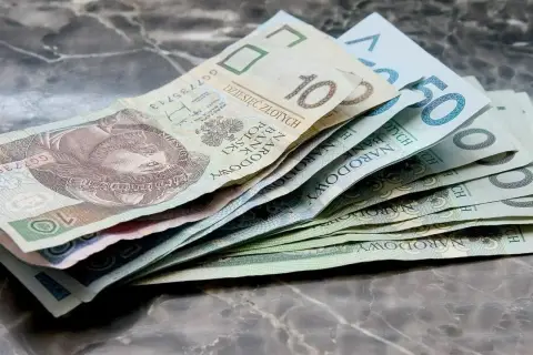 Złotówki na marmurowym blacie. Widać banknoty 10, 50 i inne, które mogą pomóc w pokryciu kosztów związanych z zasiłkiem rodzicielskim.