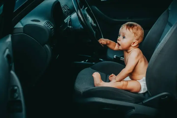 Maluch w pieluszce siedzi za kierownicą, jakby zastanawiał się, od kiedy dziecko może jeździć z przodu.