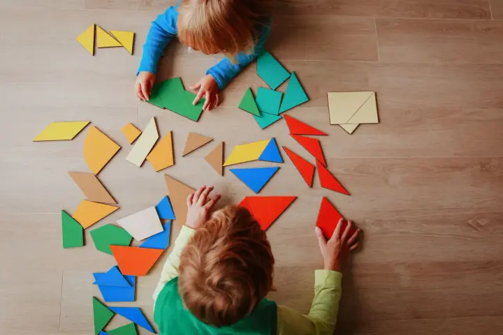Dzieci układają kolorowe klocki tangram. Widać ich skupienie podczas zabawy.